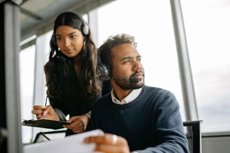 Two IT support agents wearing headsets working together at a desk
